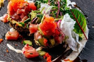 Salmon tartare with sauce and herbs on a black plate