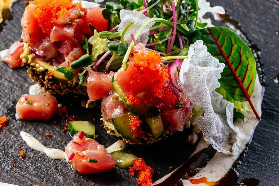 Salmon tartare with sauce and herbs on a black plate
