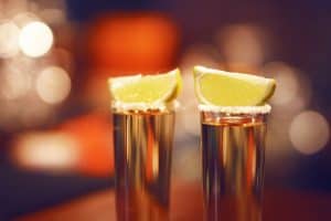 two tequila shots on a table with lime sp