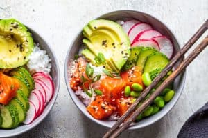 Poke bowl with salmon rice avocado edamame beans cucumber and radish in a gray bowl