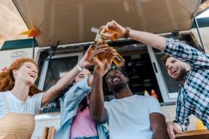 friends clinking bottles with beer near food truck