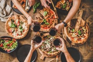 People clinking glasses with wine over table with Italian pizza