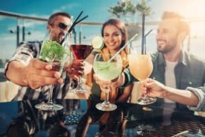 Cheerful friends holding alcohol drinks on a rooftop restaurant bar