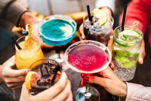 People hands toasting multicolored fancy cocktails during happy hour