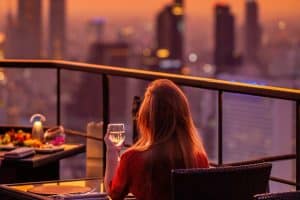 Young woman with glass of wine at luxury rooftop restaurant watching sunset