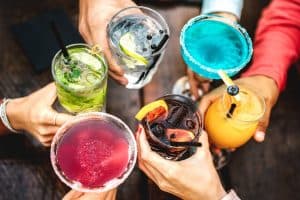 people hands toasting multicolored fancy cocktails
