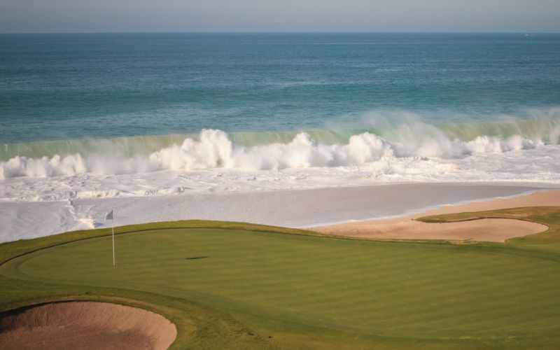 Putting green and ocean with a breaking wave in the background at a golf course in Los Cabos
