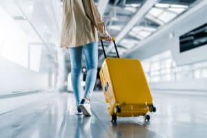 woman walking down airport with yellow carry on luggage