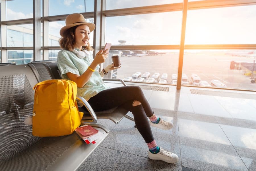 Happy asian woman waiting for her airplane in airport with passport and baggage