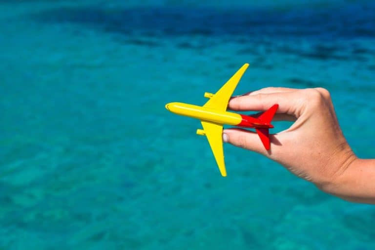 hand holding a small yellow red toy plane against tropical beach water