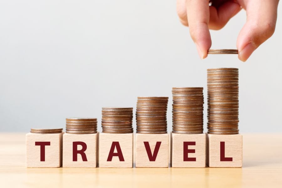 Hand putting coins on stack and wooden cube block with word TRAVEL