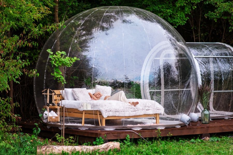 Transparent bubble tent at glamping Lush forest around and interior Woman lying on the bed and looking outside