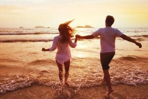 happy couple running into the shoreline during sunset