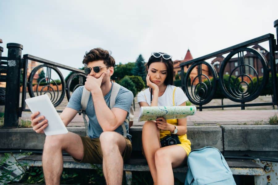 man looking at digital tablet and asian woman looking at map