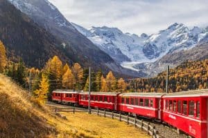 red passenger Rhaetian Railway train with Bernina massif and Morteratsch Glacier in the background Pontresina Switzerland