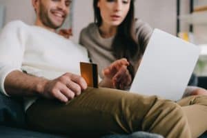 young couple shopping online with credit card and laptop on couch at home