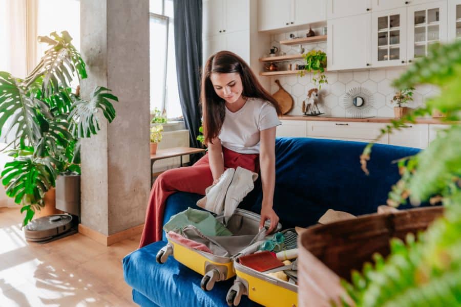 Beautiful smiling young woman packing personal belongings in a suitcase for travelling