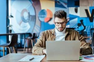 IT worker using laptop near newspaper with pen at table in coworking space