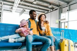 Smiling family sitting in airport with suitcase while kid holding american flag