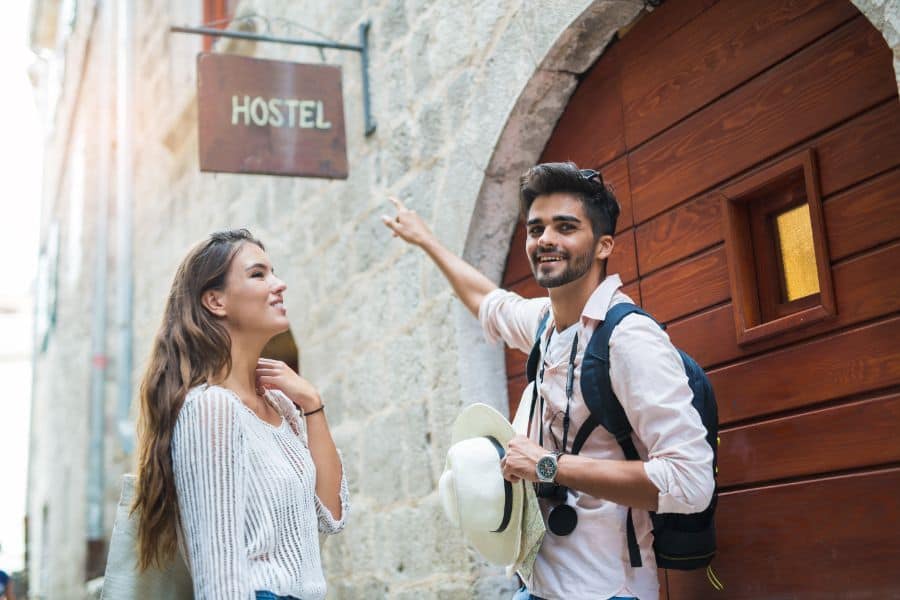 Tourist couple enjoying sightseeing and exploring city pointing at hostel sign