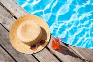 op view of wicker hat sunglasses and bottle with summer drink near swimming pool