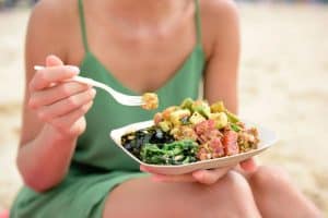 Woman sitting on beach eating hawaiian poke lunch