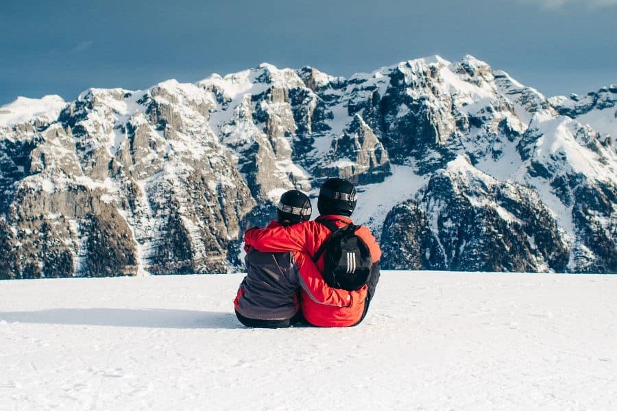 couple sitting on top of snow covered mountain slope sp