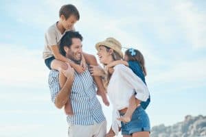 a happy young couple carrying their two children during an enjoyable day on the beach