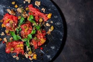 Fresh beef carpaccio with capers mustard and arugula on black board top view