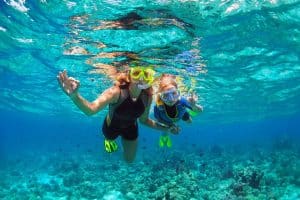 Mother kid in snorkeling mask dive underwater with tropical fishes