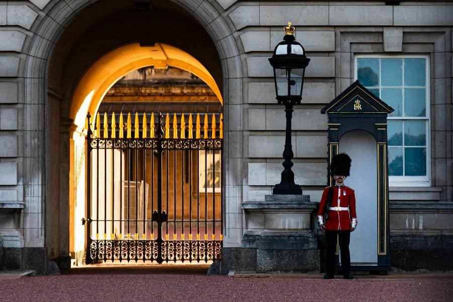 a guard stands in front of a gated entrance buckingham palace sp