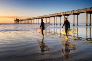 two person walking on the seaside holding surfboards san diego sp