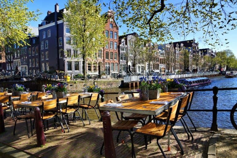 Restaurant tables lining the beautiful canals of Amsterdam under blue skies during springtime Netherlands